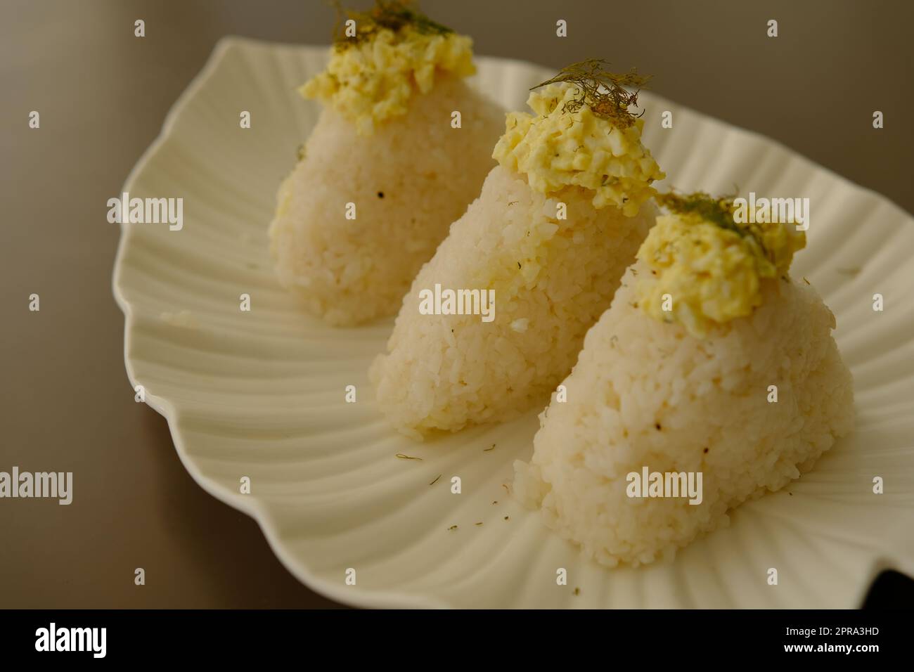 Plate with traditional Japanese onigiri with egg on brown background and beautiful white plate with leaf shape Stock Photo