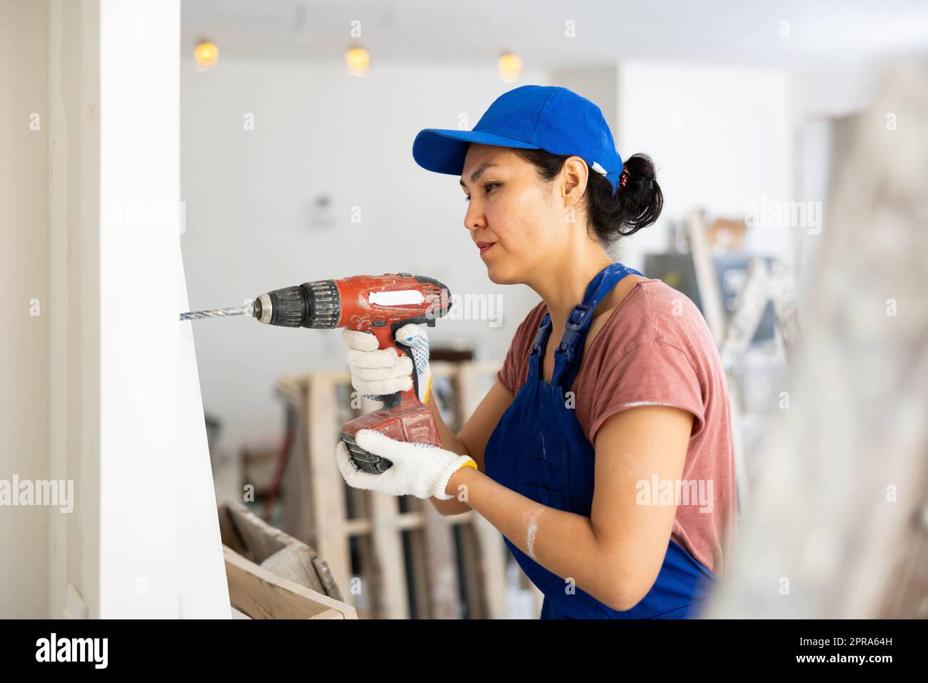 Woman builder using drill to bore hole in wall Stock Photo