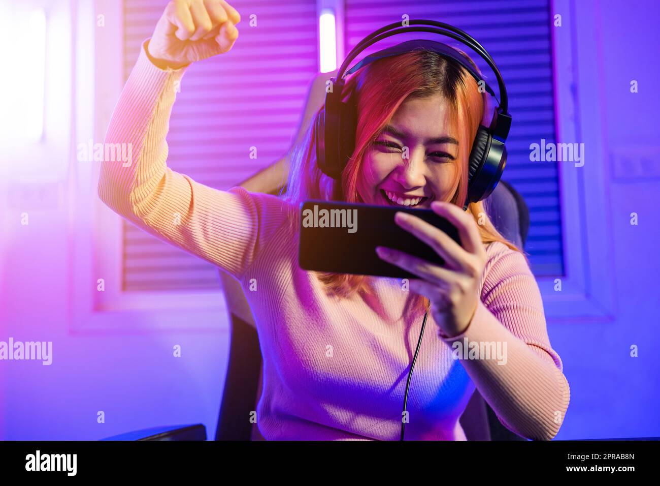 Happy Gamer playing video game online with smartphone she raises hands