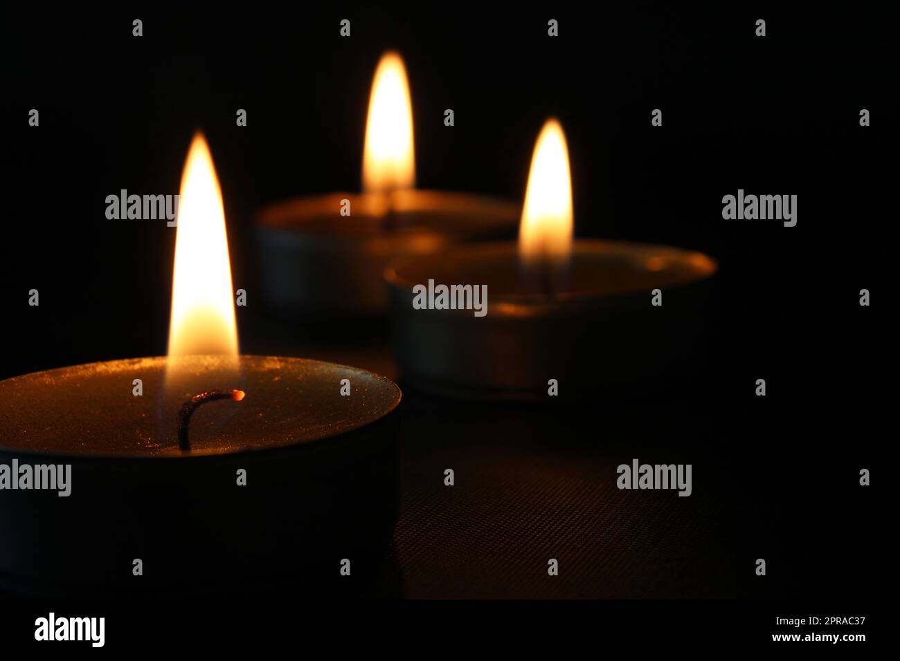 Three burning candles closeup on a black background with copy space