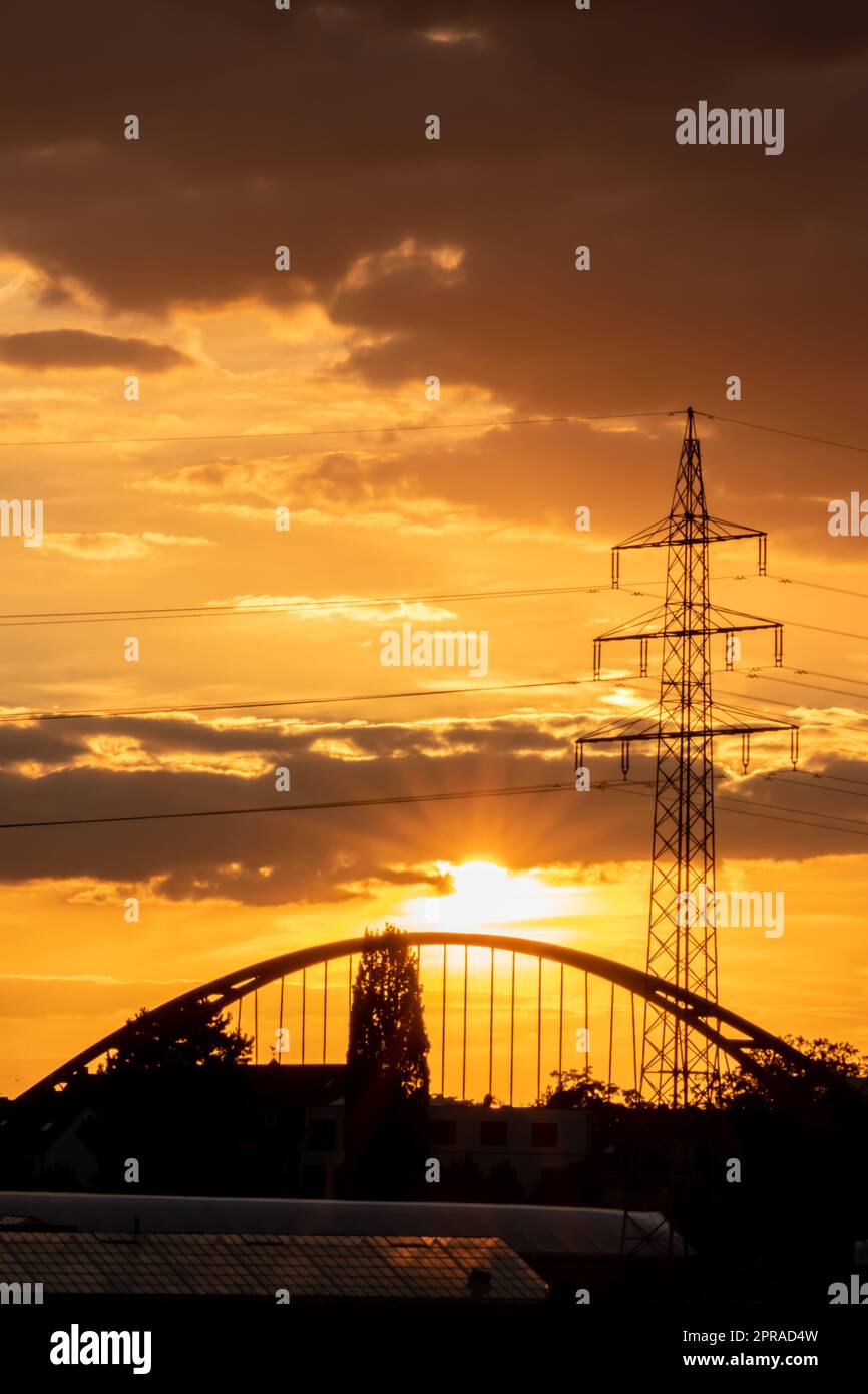 Golden sky with sun rays and lens flare shows solar energy with electricity tower pylon silhouette in golden sunset and orange sky for sustainable energy or renewable resources from dusk till dawn sun Stock Photo