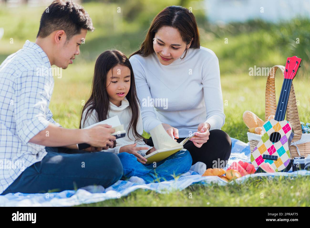 Asian family having fun and enjoying outdoor on picnic blanket reading book in park Stock Photo