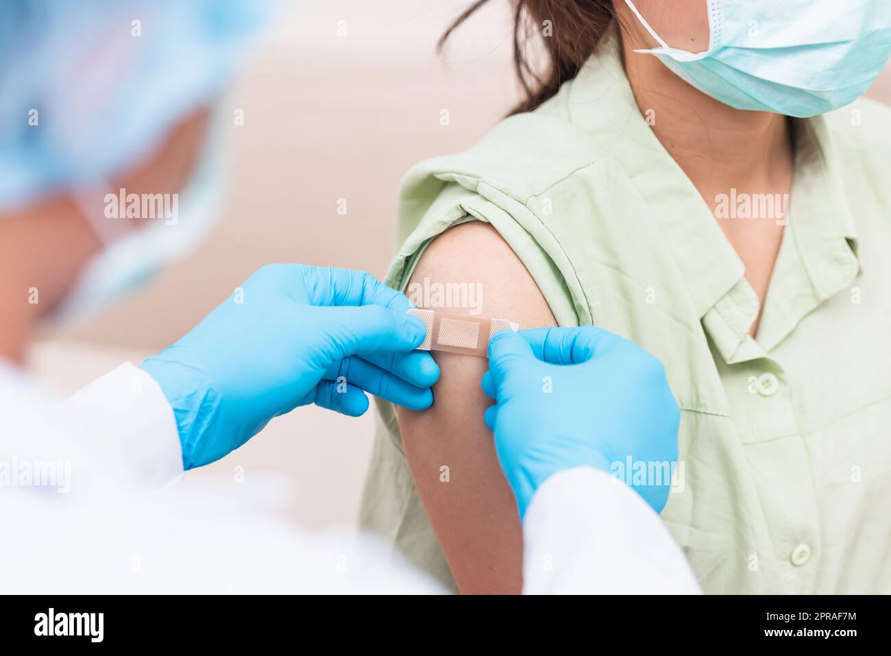 Doctor man after injection coronavirus vaccine to young woman shoulder he rubber protective gloves putting an adhesive bandage plaster Stock Photo