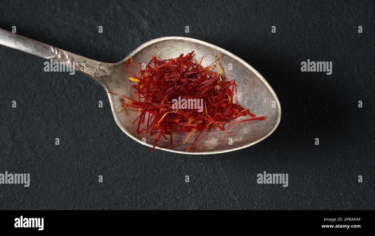 Expensive Red Dried saffron spice in a spoon on dark background Stock