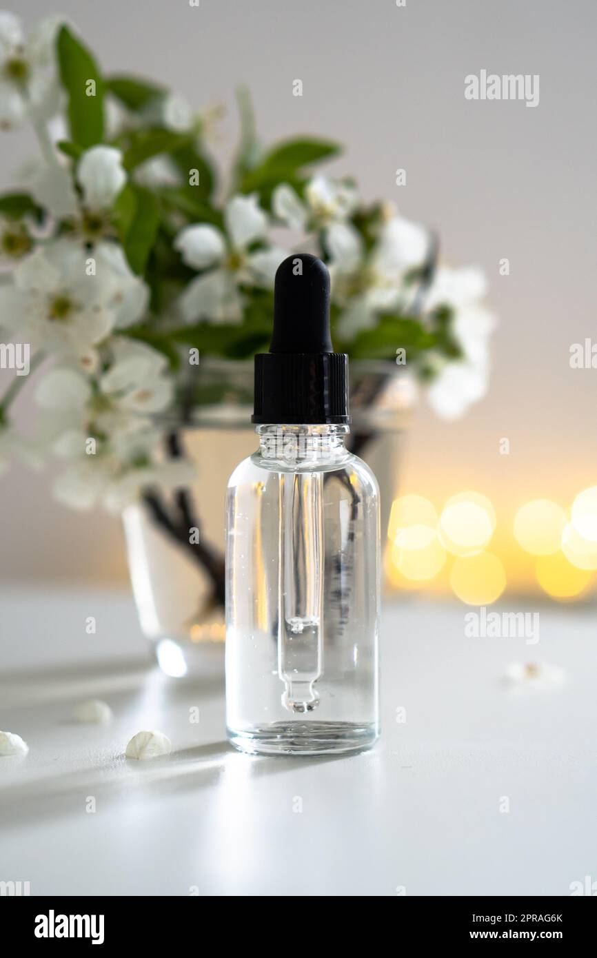 Clear glass cosmetic dropper bottle and white cherry flowers with bokeh ...