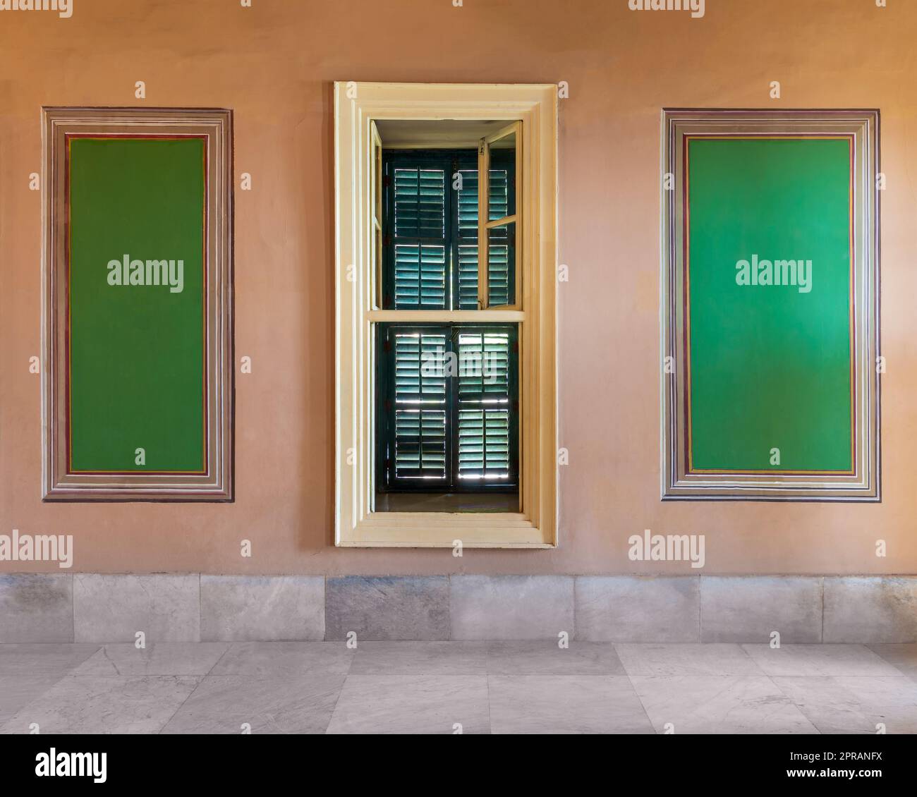 Wooden window with green shutters mediating elegant rectangular green frames on orange wall Stock Photo