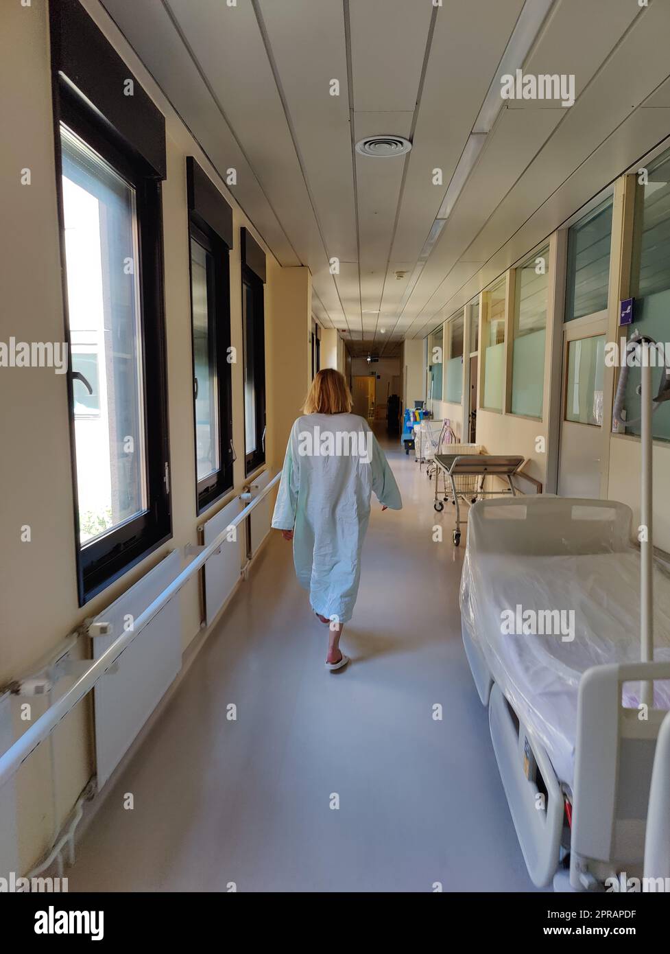 Female patient wearing hospital robe walking in long empty hospital