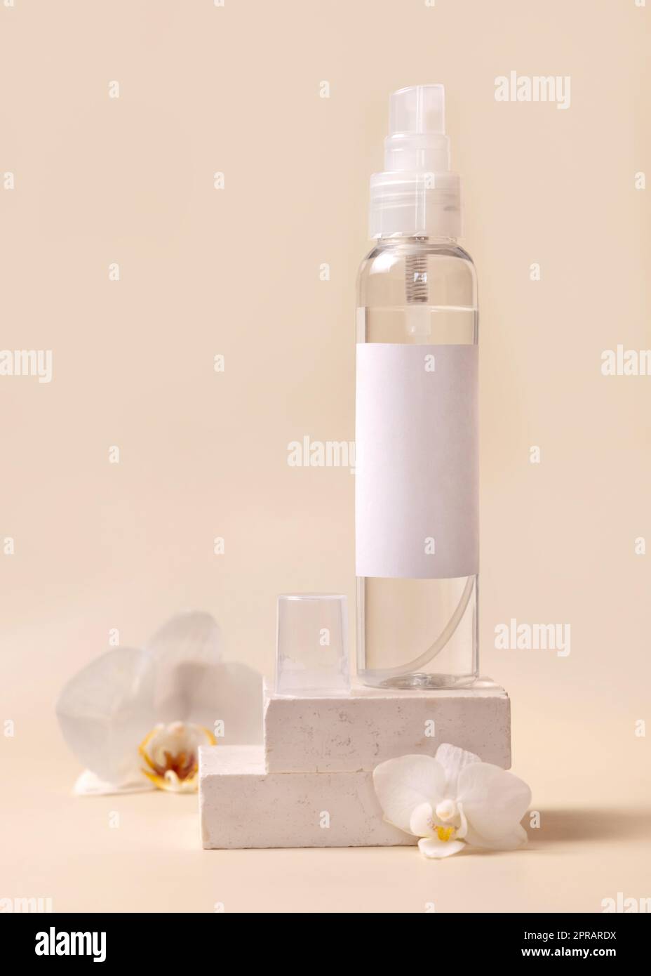 Spray dispenser bottle near white orchid flowers and stones on light beige close up, Mockup Stock Photo