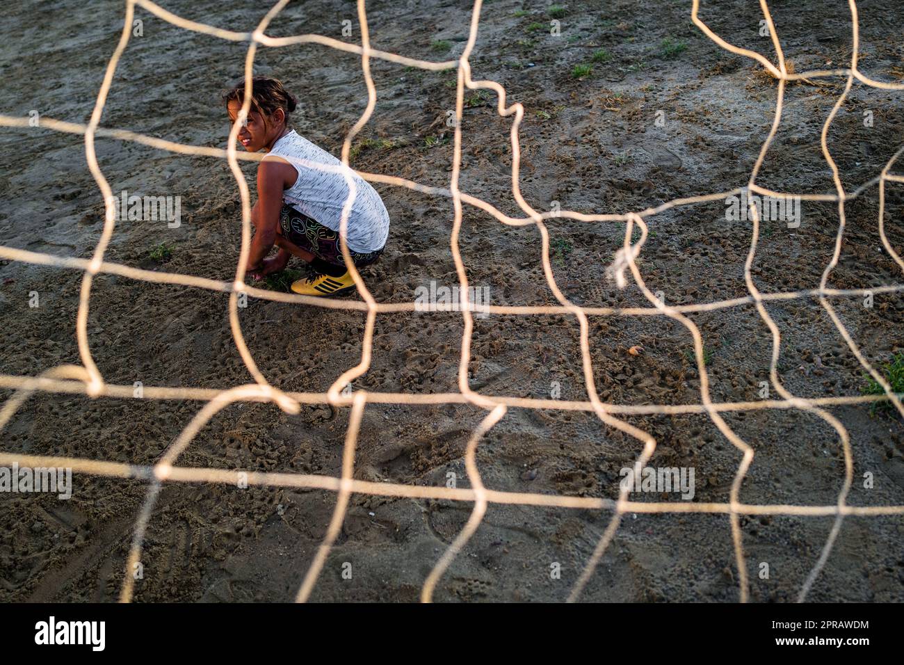 A young Colombian female football player sits inside the goal during a training session on a dirt playing field in Necoclí, Antioquia, Colombia. Stock Photo