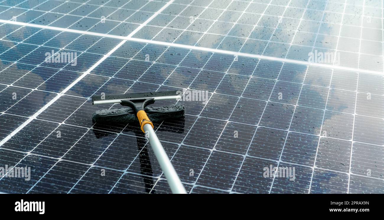 Cleaning solar panel with microfiber mop on wet roof. Solar panel or photovoltaic module maintenance service. Sustainable resource. Solar power. Green energy. Sustainable development technology. Stock Photo
