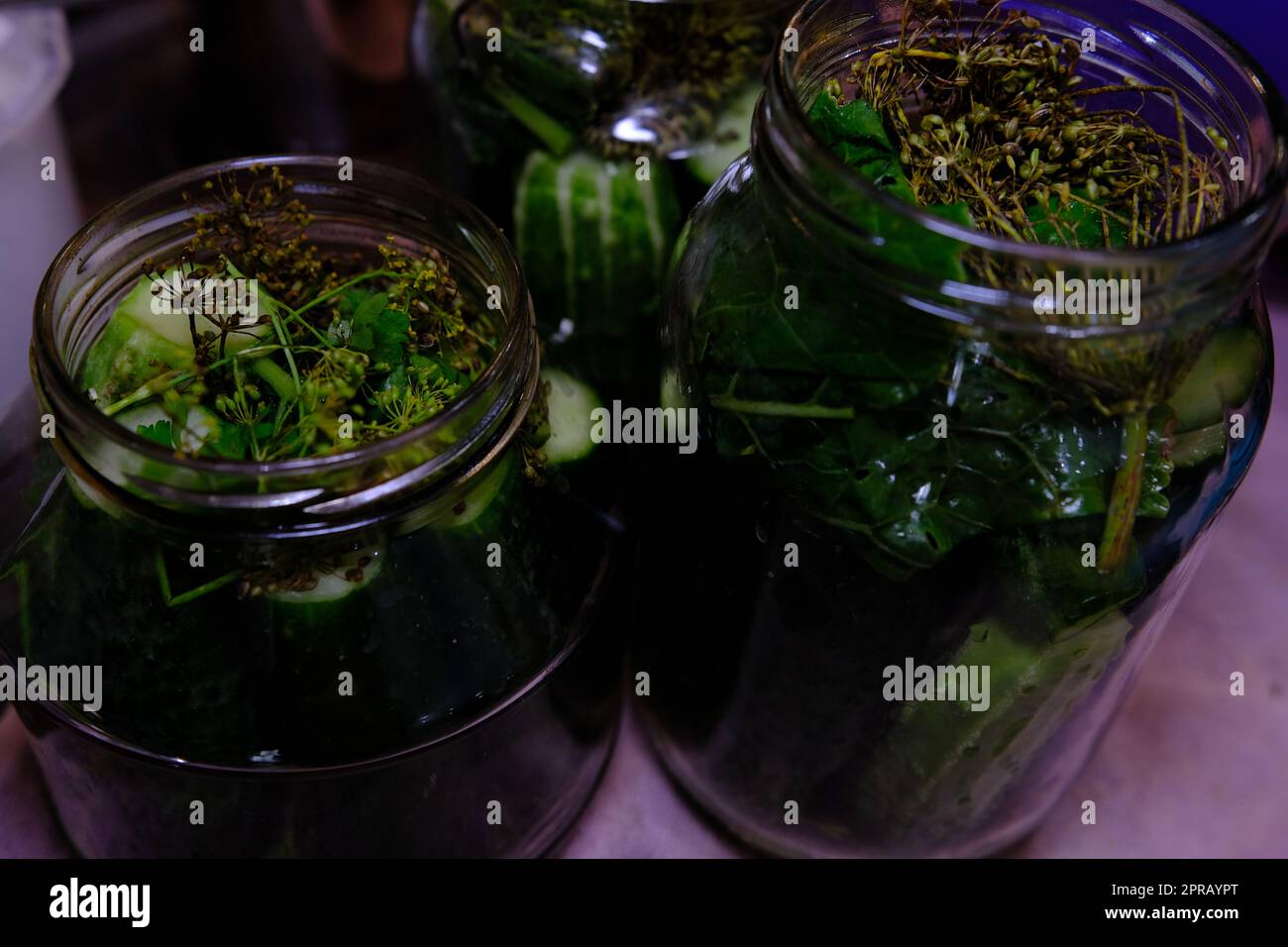 homemade canned cucumbers in big and small glass jars stand on kitchen table against Stock Photo