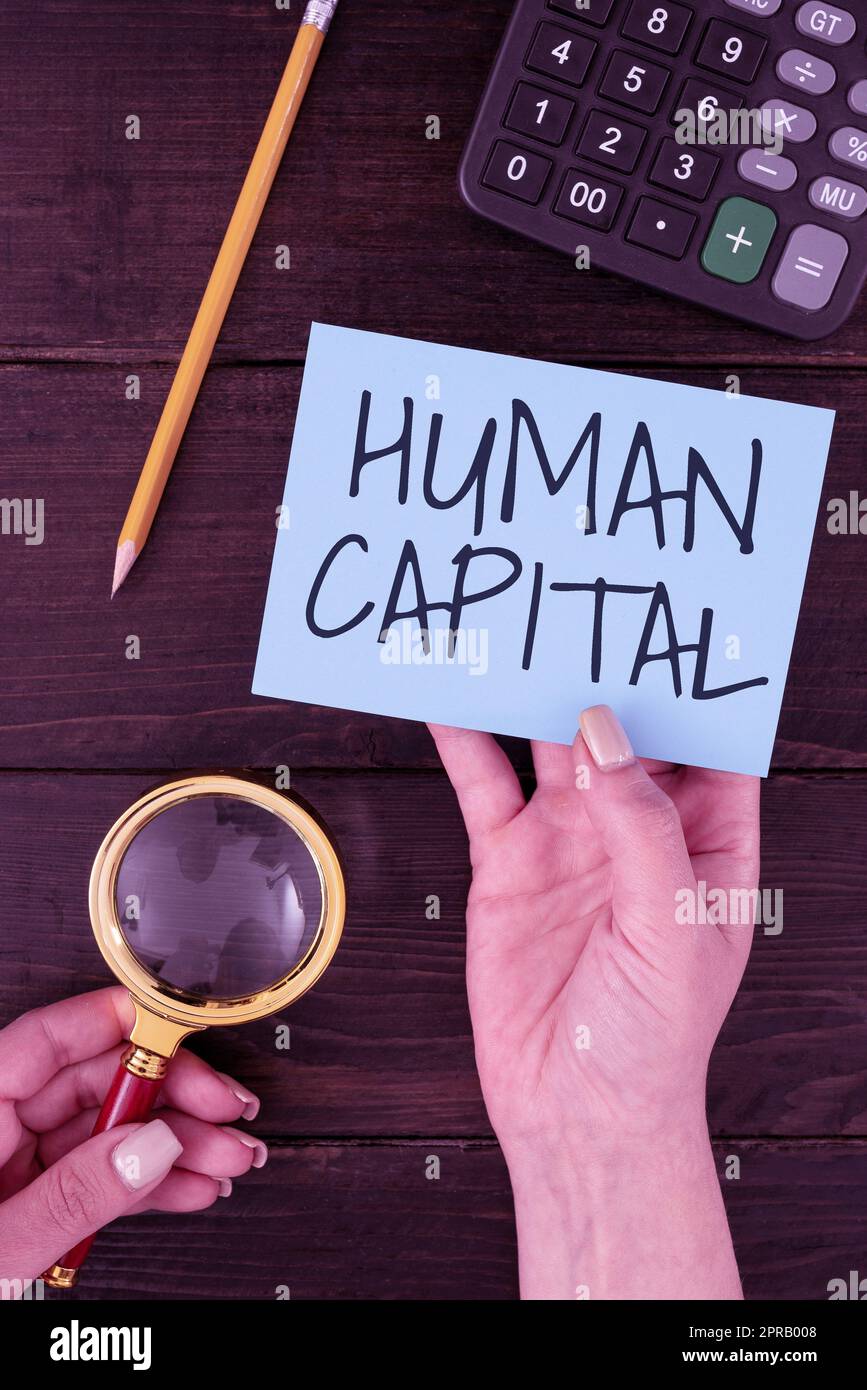 Handwriting text Human Capital. Concept meaning Intangible Collective Resources Competence Capital Education Hands Of Woman With Blank Paper And Stationery For Advertisement. Stock Photo