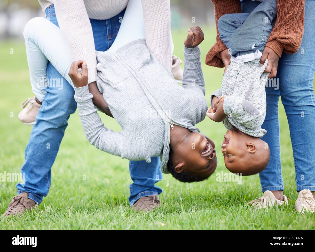 Fun is the absence of stress. two children hanging upside down by their parents outside. Stock Photo