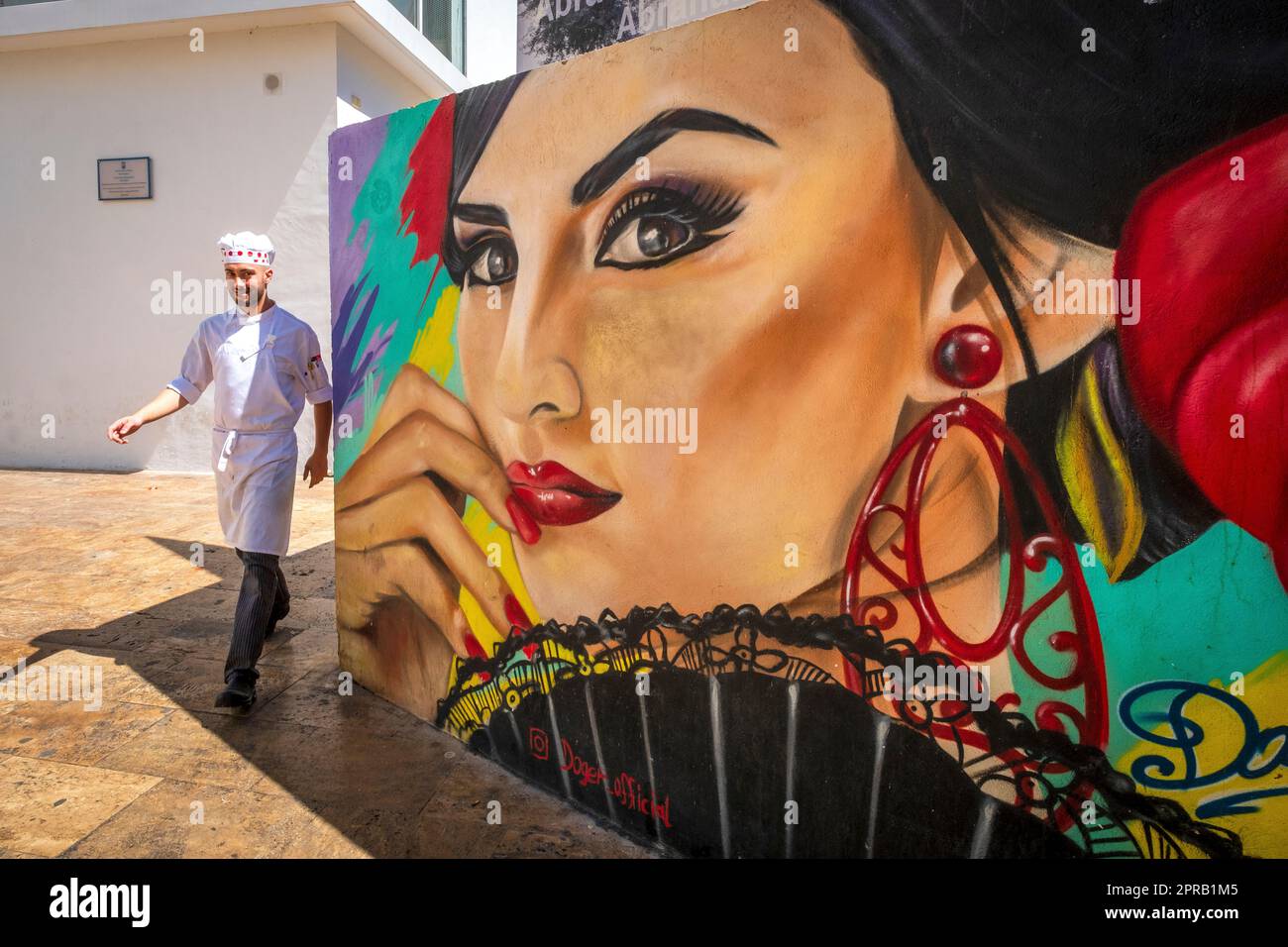 A waiter walks around a corner in Málaga, Spain;  mural of a Spanish woman wearing earrings Stock Photo