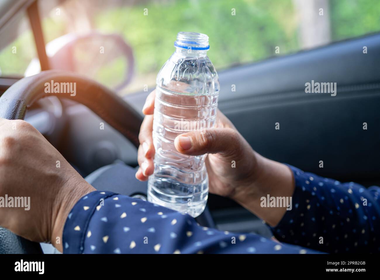 Asian woman driver holding bottle for drink water while driving a car. Plastic hot water bottle