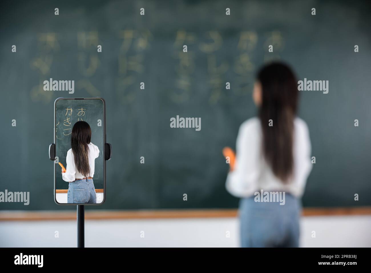 Asian teacher teach on board while have blackboard lecture online through smartphone in classroom Stock Photo