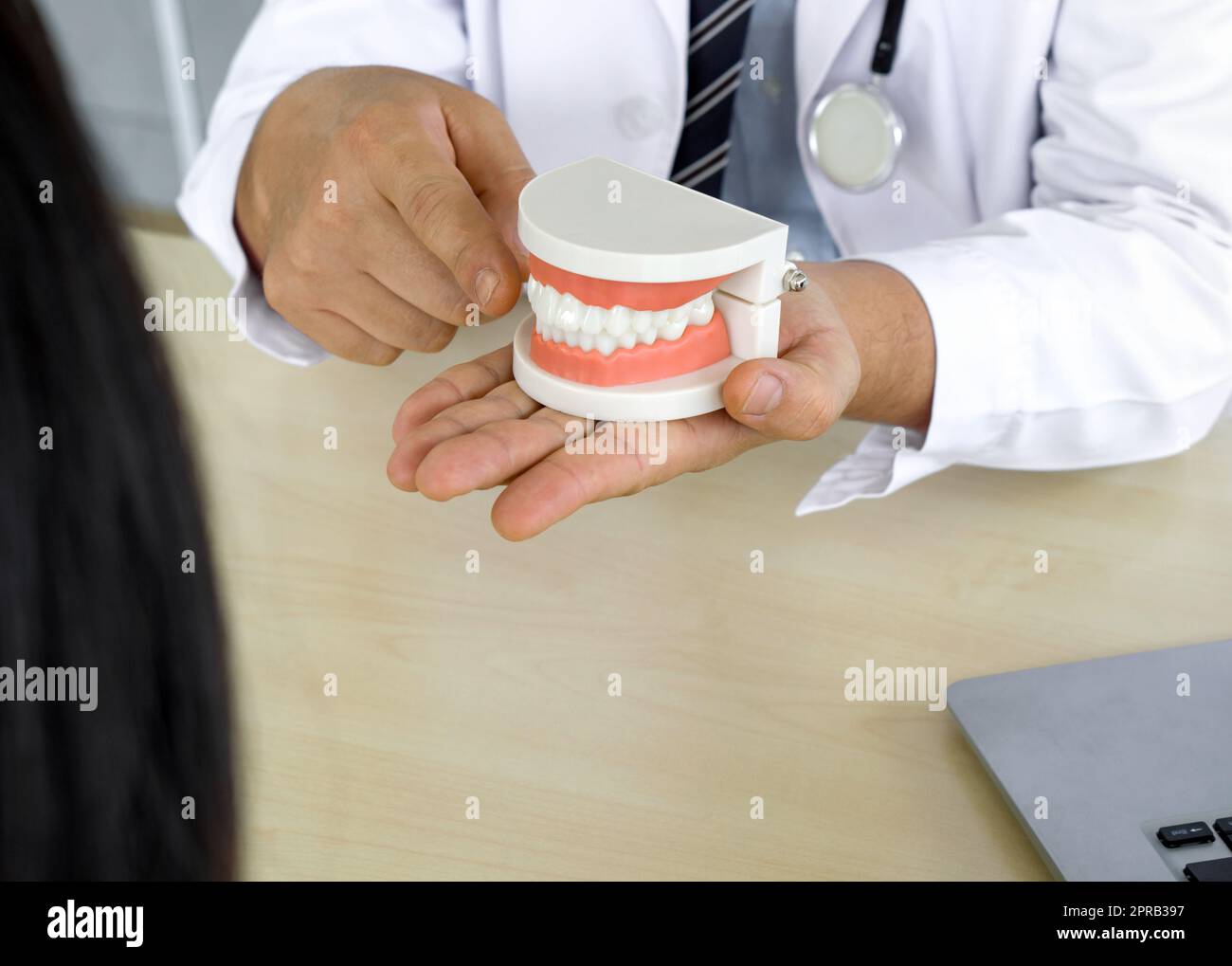 Dentist in white gown and stethoscope pointing finger at tooth model