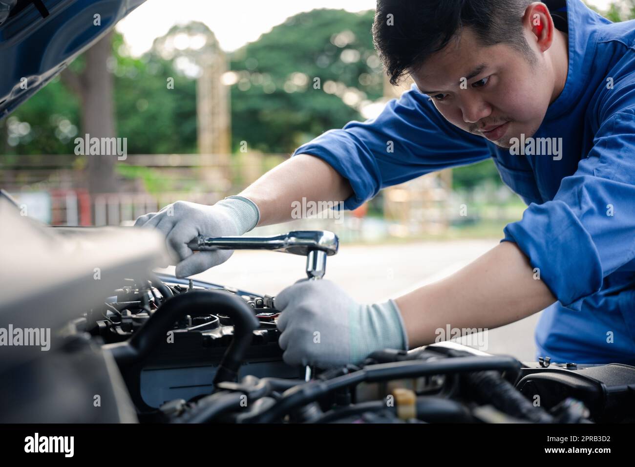 Asian auto mechanic man working on car engine using wrench to repair and maintenance Stock Photo