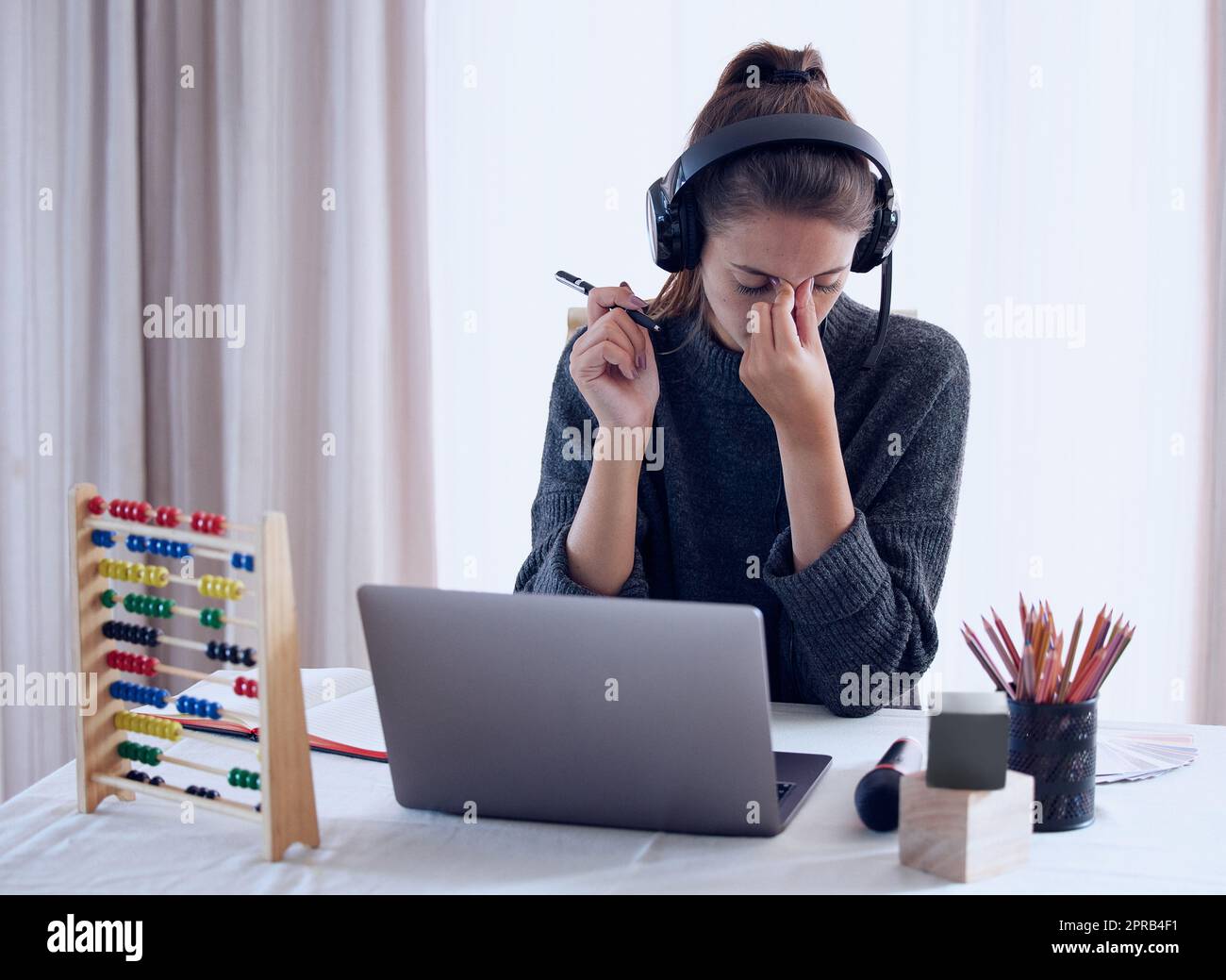 Burnout can be prevented with proper self-care. a young getting a headache while teaching an online lesson with her laptop at home. Stock Photo
