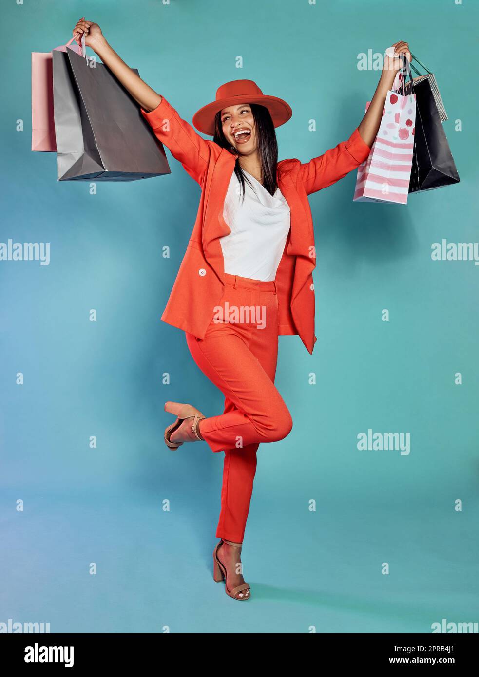 Excited and trendy woman with shopping bags after retail therapy, spending and buying clothes. Stylish, edgy and funky model holding gifts and wearing colorful, fashionable red suit while happy Stock Photo