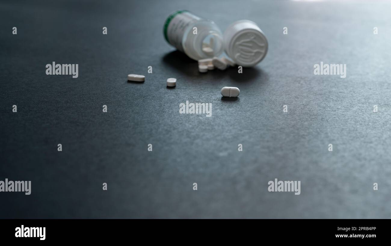 White tablets pills and blur plastic pill bottle on dark floor. Prescription drugs. Pharmaceutical industry. Medical care. Medication for cure illness. Pharmacy. Small white pills. Dose recommended. Stock Photo