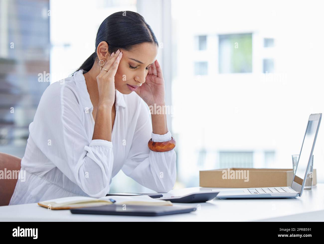 In solitude without rescue. a young businesswoman sitting at a desk suffering a migraine in a modern office. Stock Photo