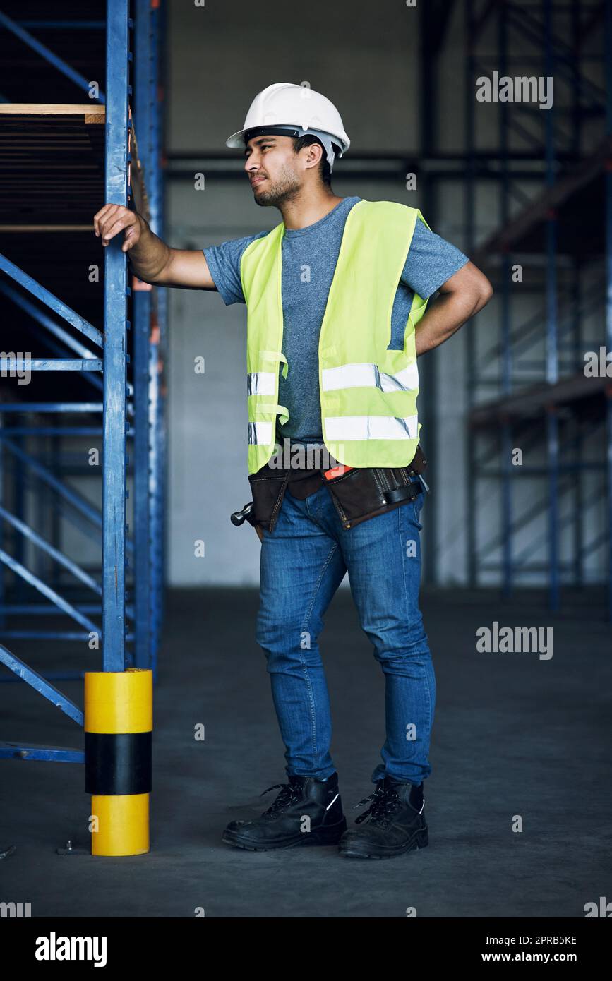 Hard work has rewards but it also has its risks. a young man experiencing back pain while working at a construction site. Stock Photo