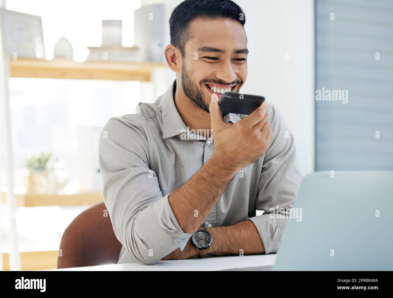 Funny voice notes are the order of the day. a young man using his cellphone at work in a modern office. Stock Photo