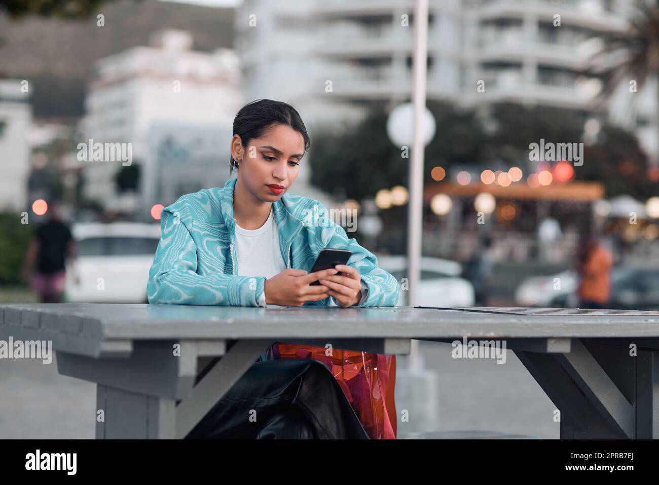 Edgy, sad and lonely woman texting on social media dating app on a phone and looking serious, depressed or bored outside in an urban city. A single girl posting about her bad emotional breakup online Stock Photo