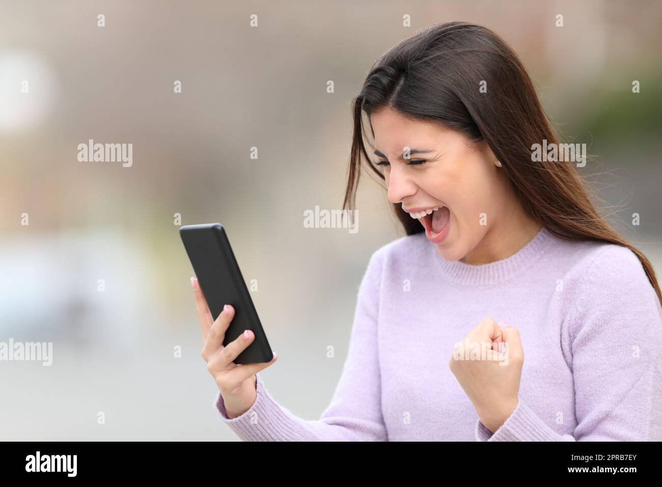 Excited teen reading phone content in the street Stock Photo