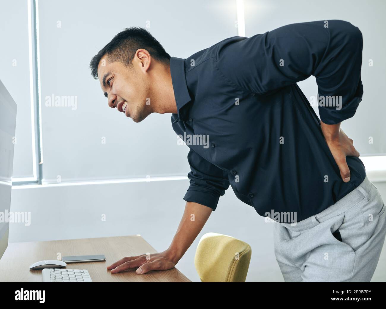 Why does my back have to age first. a handsome young businessman standing alone in his office and suffering from back ache. Stock Photo