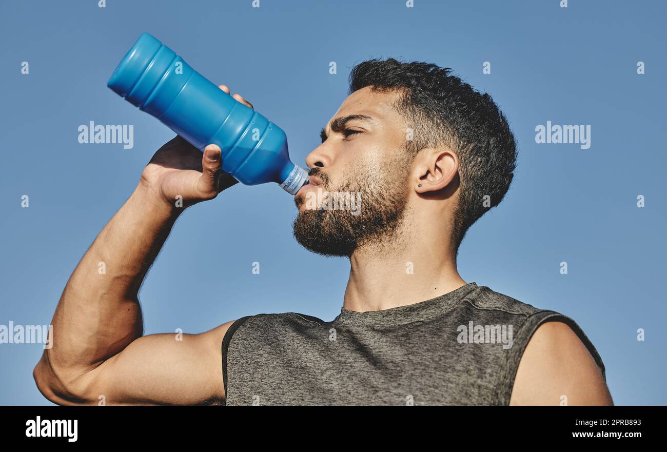 Woking up a thirst after an intense workout. Low angle shot of a sporty young man drinking water while exercising outdoors. Stock Photo