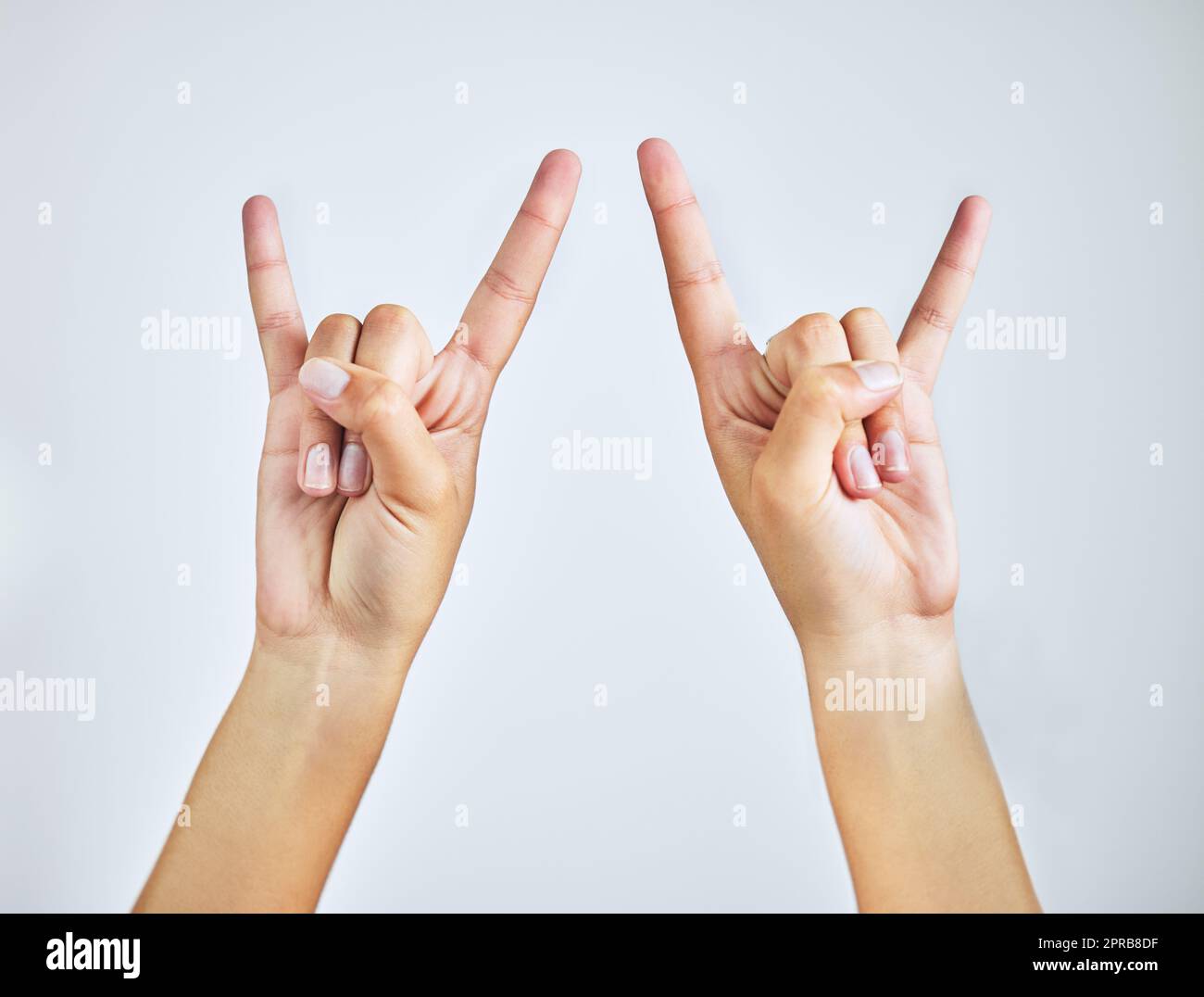 Rock on. Studio shot of a woman making a rock n roll gesture against a grey background. Stock Photo