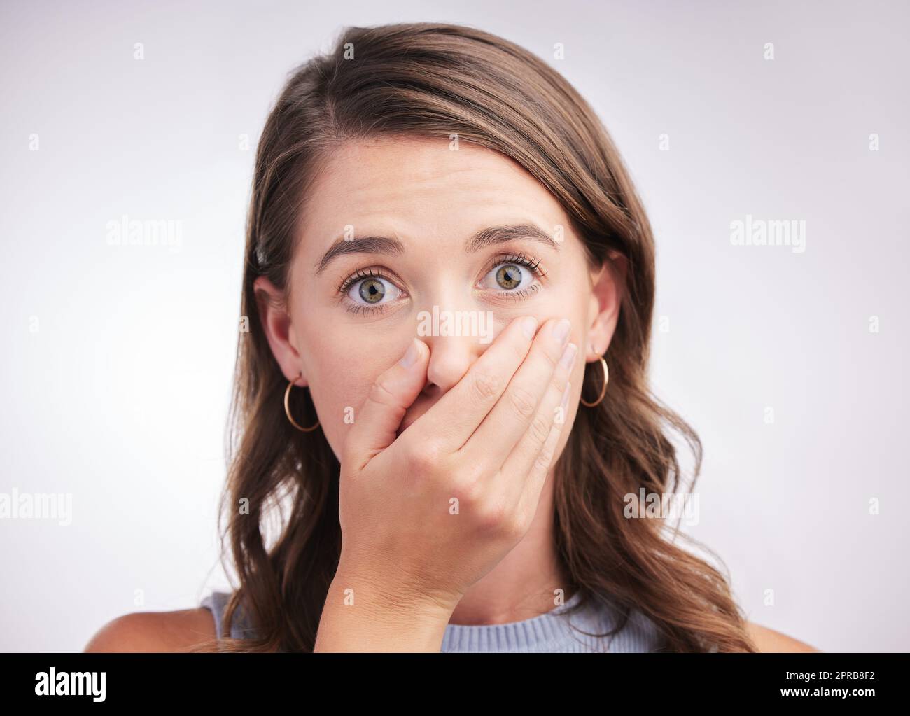 Well thats a bit awkward... Studio portrait of a young woman looking surprised against a grey background. Stock Photo