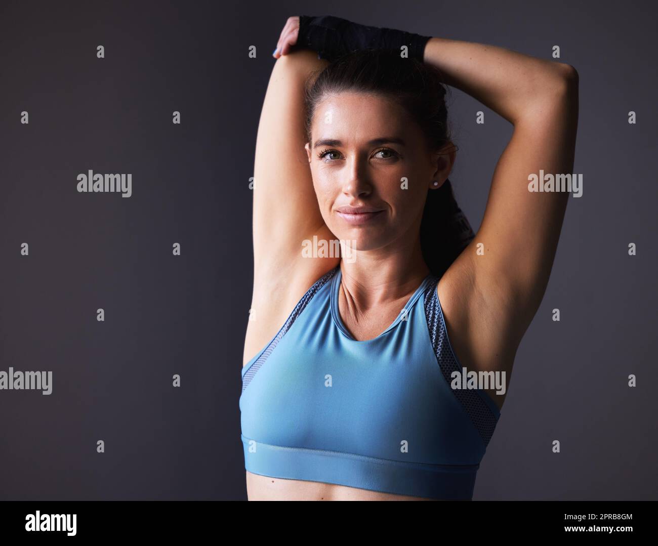 Im so ready to prove my strength. a young woman stretching her arms against a grey background. Stock Photo