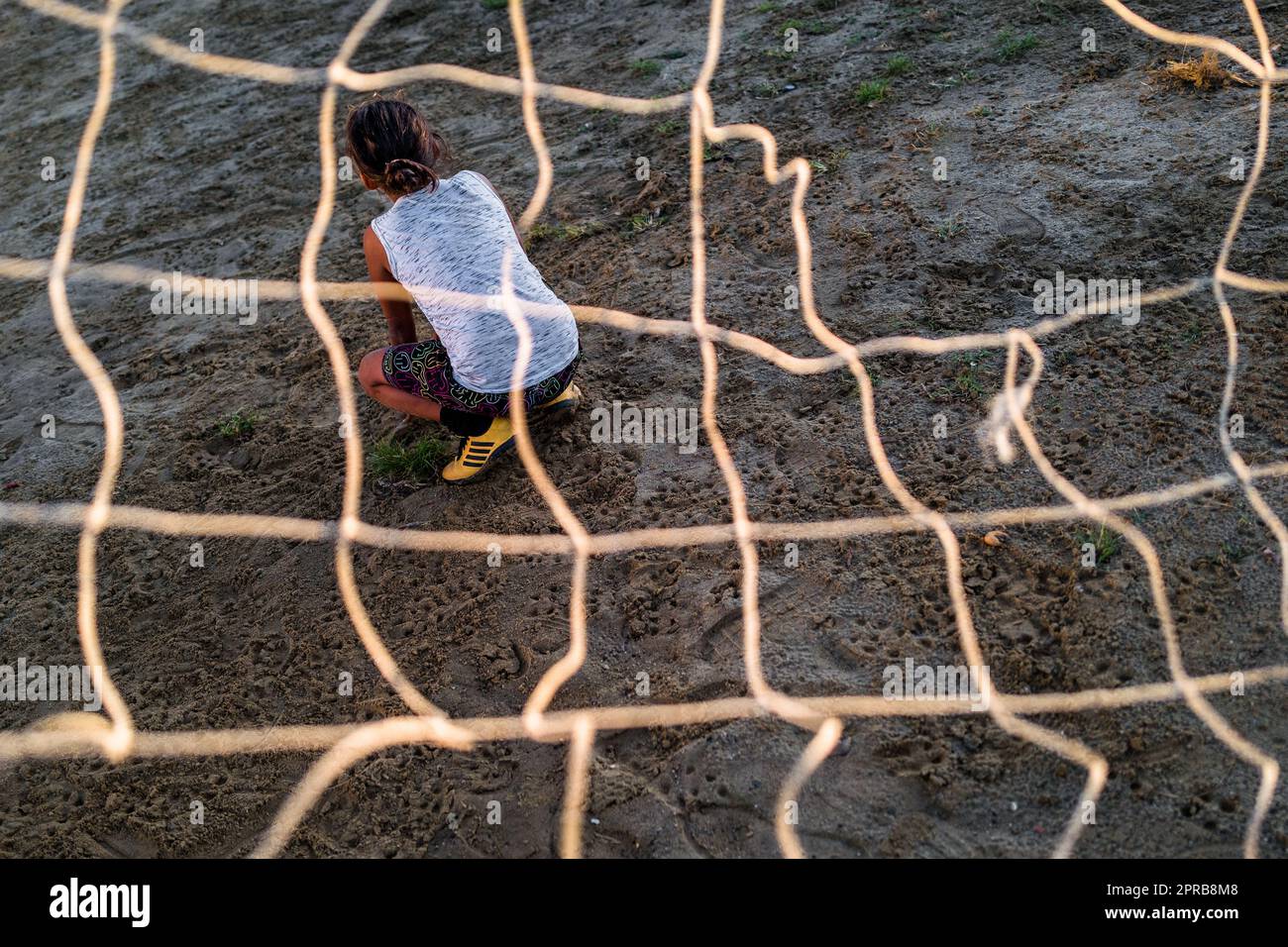 A young Colombian female football player sits inside the goal during a training session on a dirt playing field in Necoclí, Antioquia, Colombia. Stock Photo