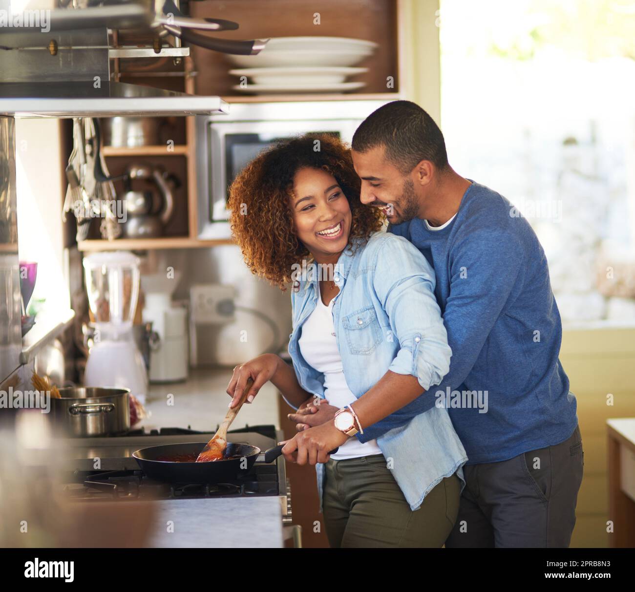 Dinners almost done my love. Shot of a young man hugging his wife while she prepares a meal at home. Stock Photo