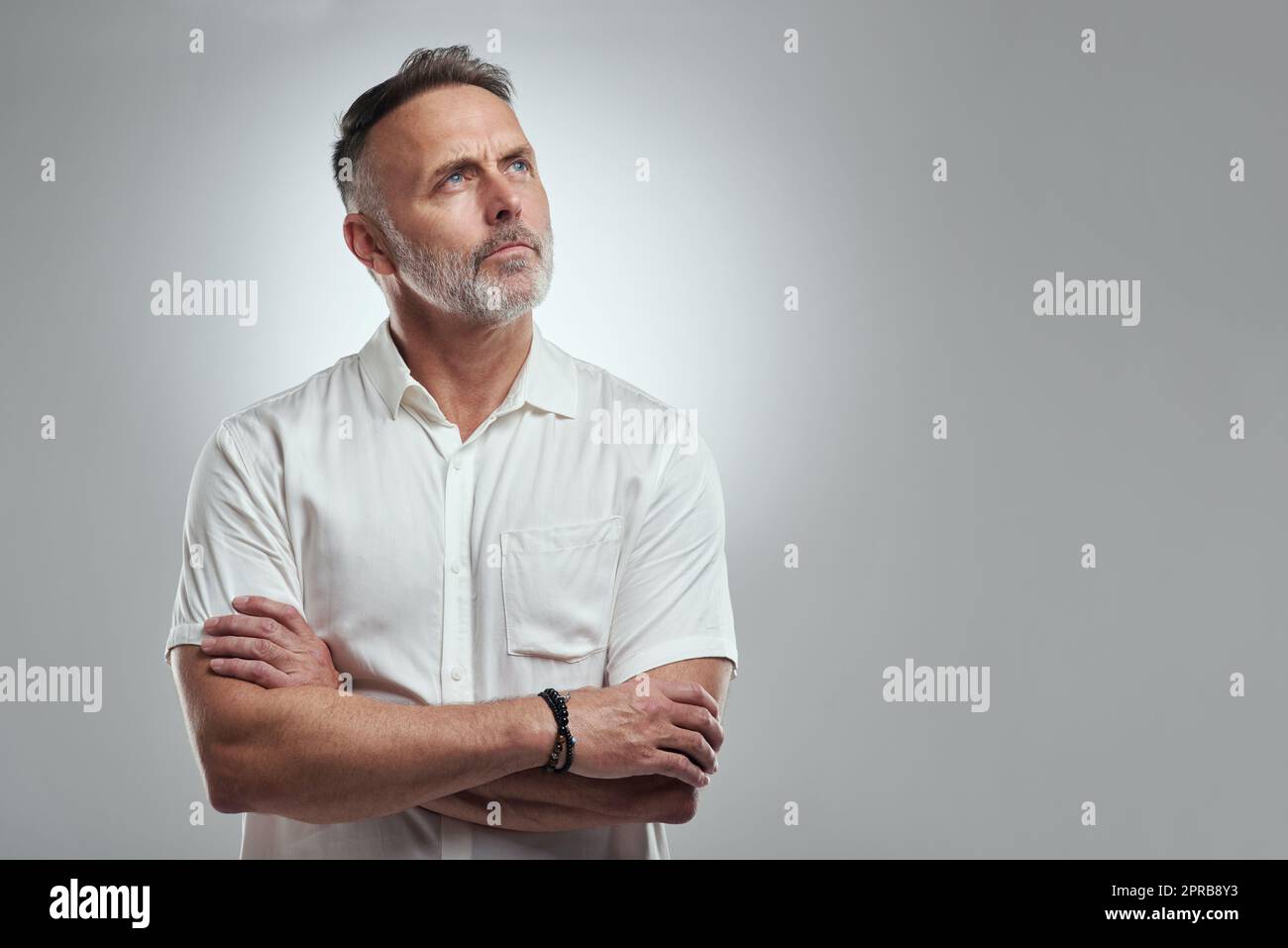 My brain doesnt like to be quiet. Studio shot of a mature man looking thoughtful against a grey background. Stock Photo
