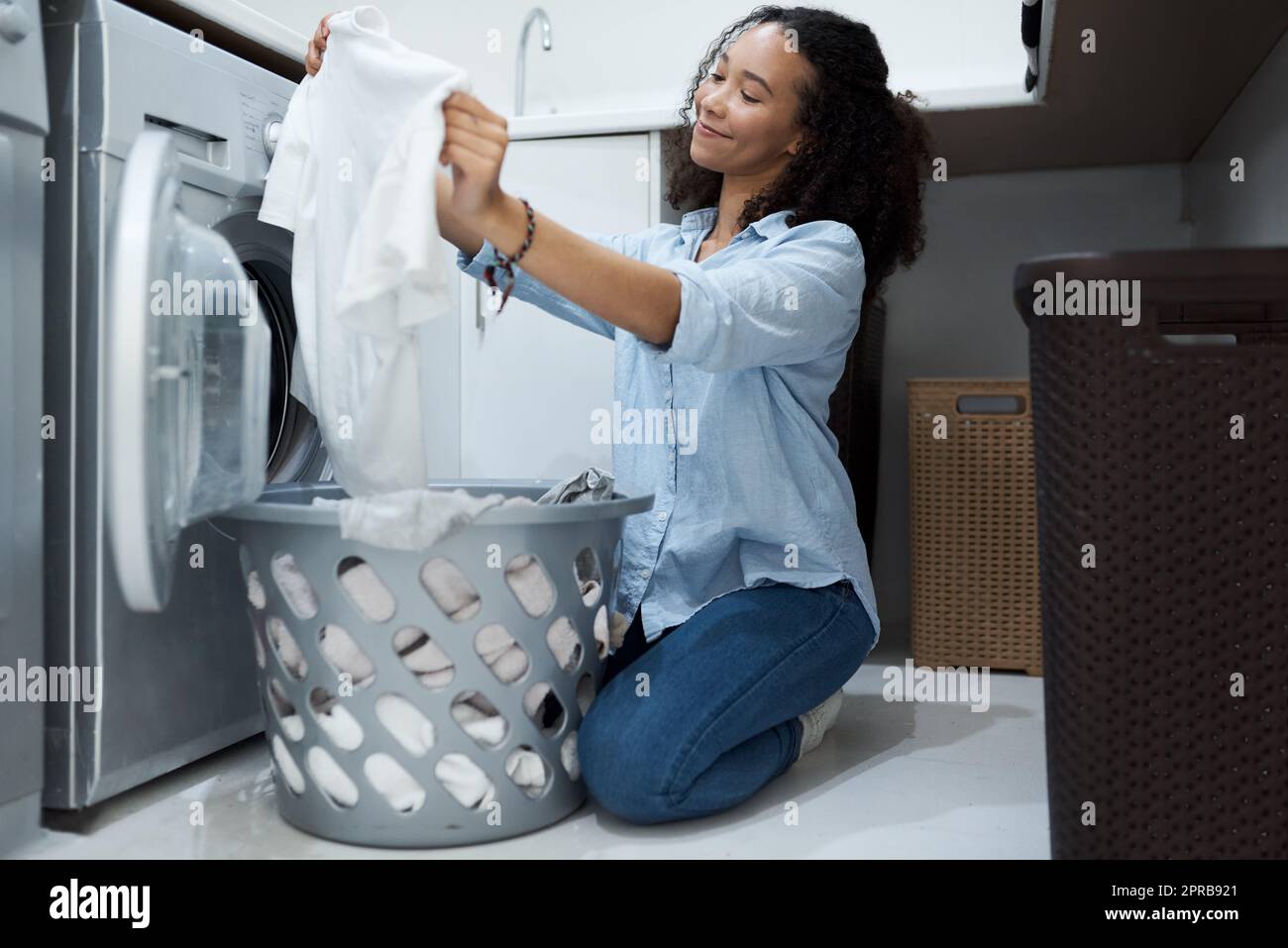 This washing powder really makes clothes sparkle. a young woman preparing to wash a load of laundry at home. Stock Photo