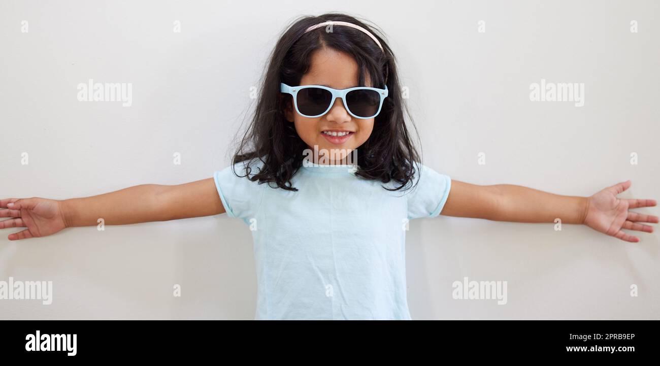 Im not just a little cute, Im this much cute. an adorable little girl wearing sunglasses while standing against a wall. Stock Photo