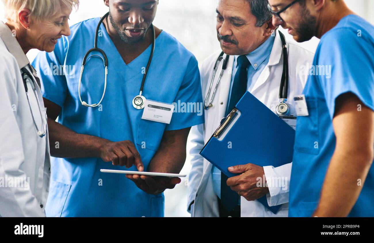 Group of doctors, medical professionals and workers doing reaching on a tablet, browsing on the internet and discussing a health case together at a hospital. Experts talking about a diagnosis Stock Photo