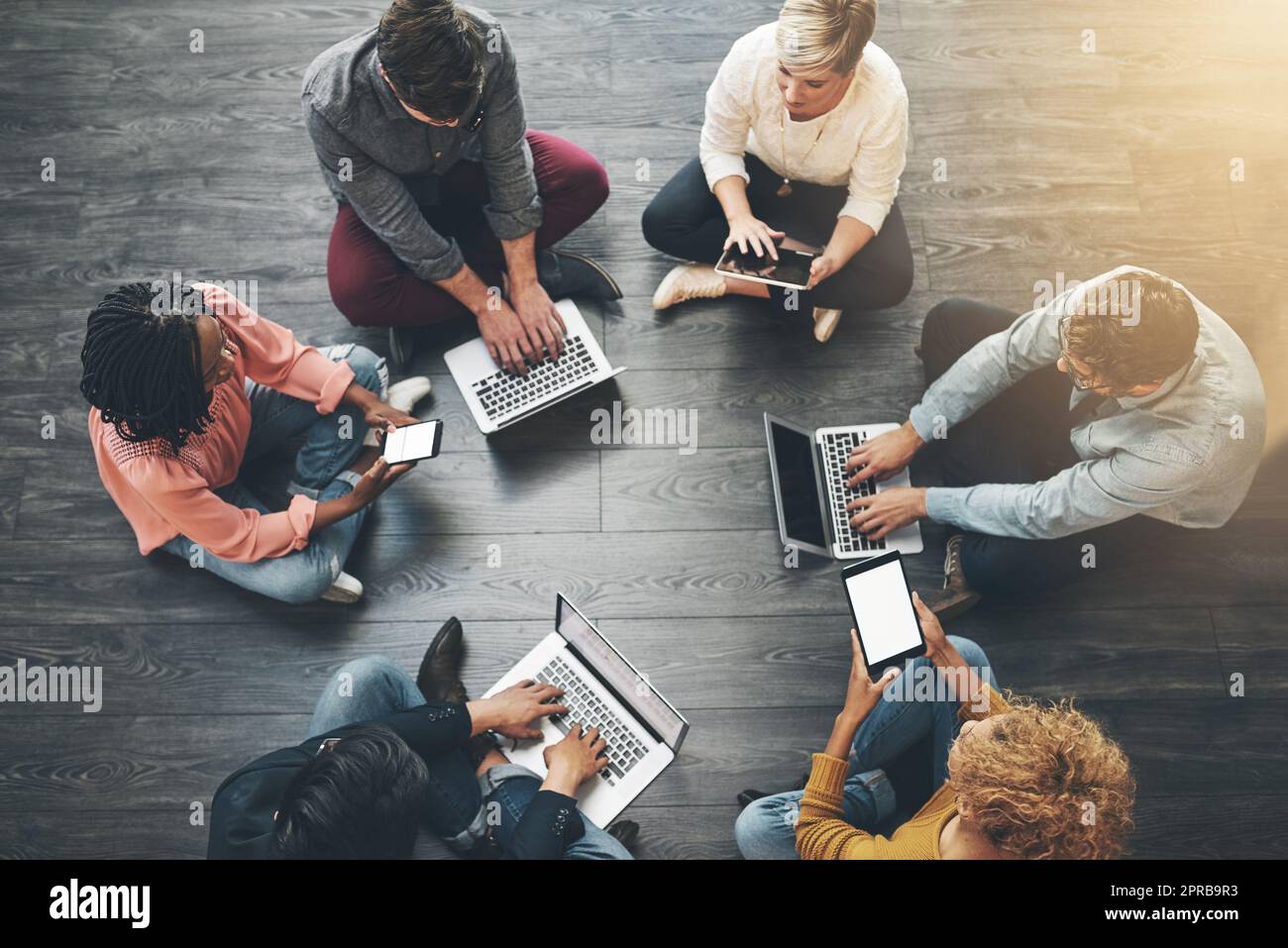 Creative, modern group of casual business people, sitting with laptop and brainstorming on presentation meeting. Overhead view of team of employees sitting on office floor, working on ideas together Stock Photo