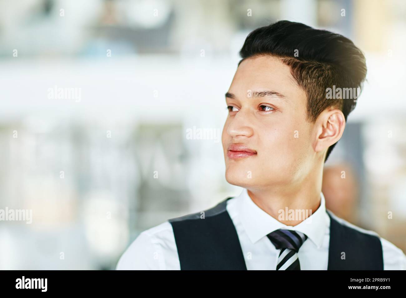 Young professional waiter, bartender or host looking confident, serious and wearing formal uniform on a blurred background. Closeup side profile, head and face of a man working in hospitality Stock Photo