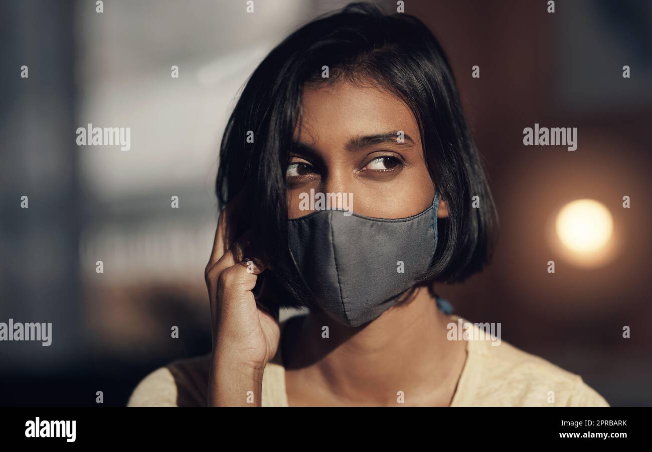 To wear or not to wear Is that even a question. a young woman wearing a face mask and looking thoughtful. Stock Photo