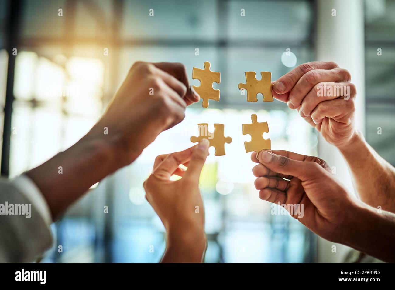 Group of business people holding puzzle pieces. Professionals connect and collaborate together inside office building. Closeup of hands, and team working together on a new strategy for success. Stock Photo