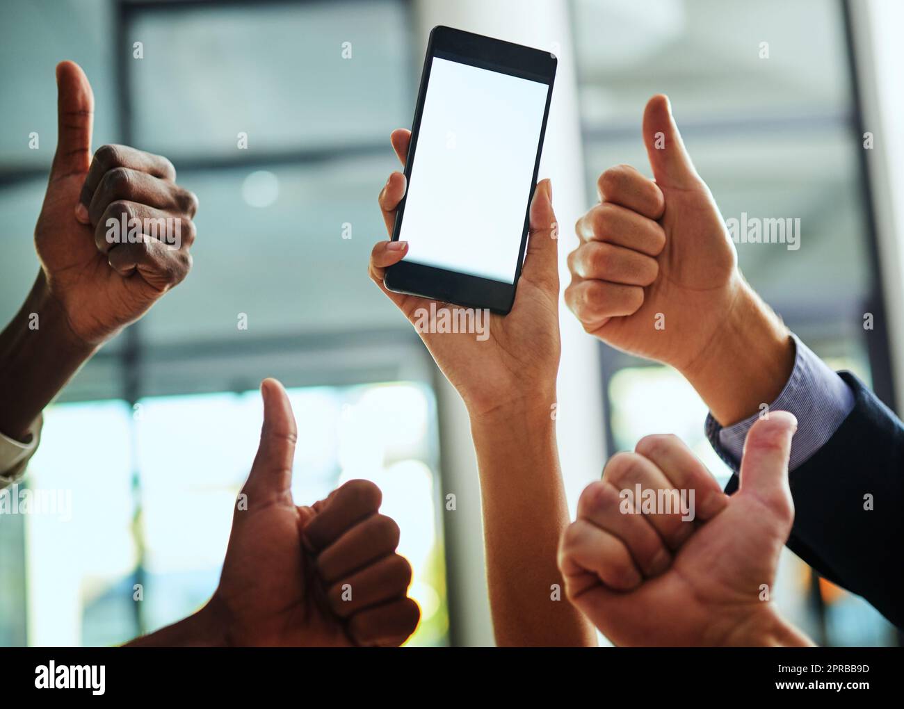 Thumbs up, support and blank phone screen shown by professional corporate business people in an office together. Employees and colleagues showing agreement while holding a device with information Stock Photo