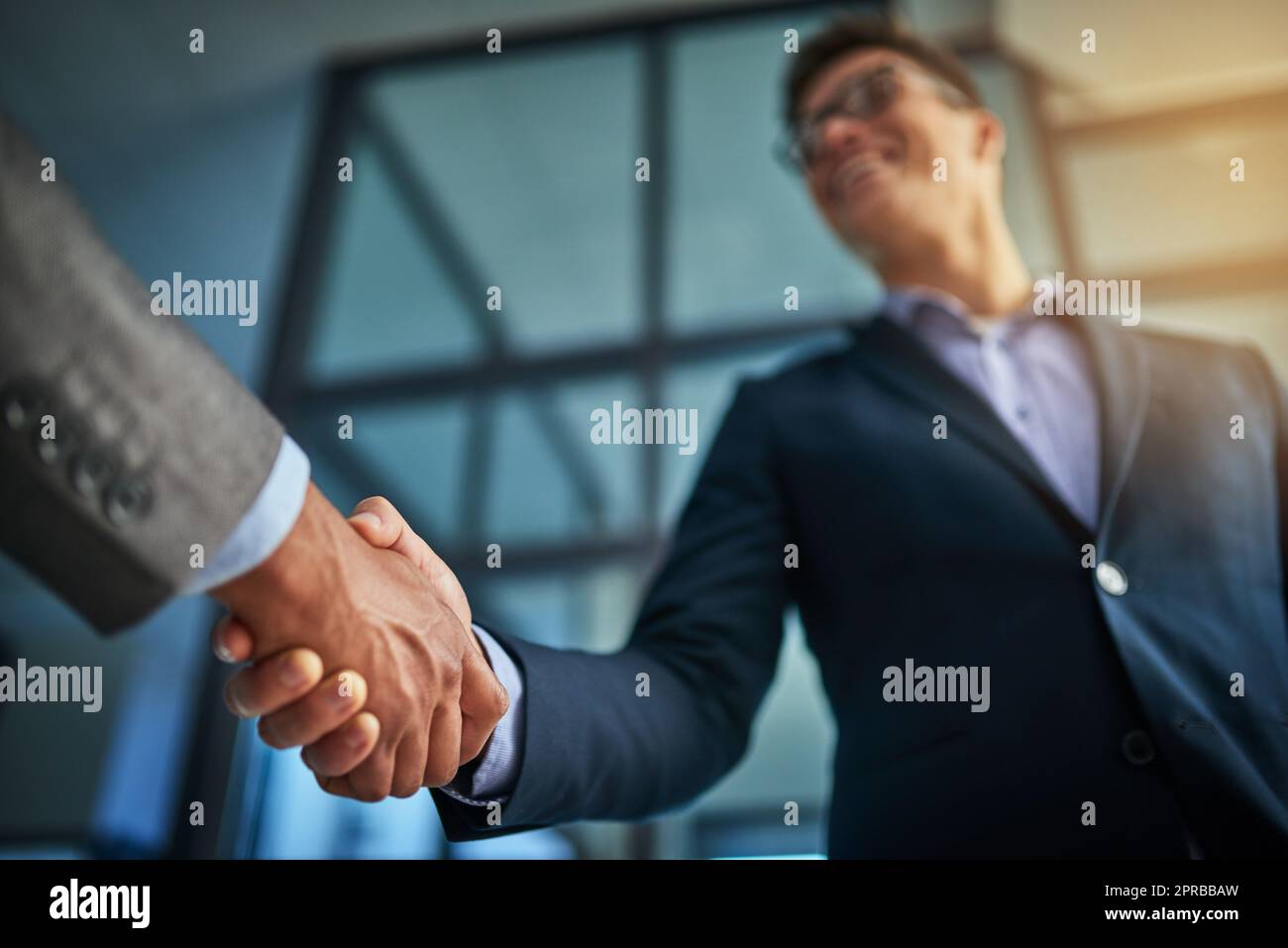 A professional handshake after a successful group collaboration meeting after in a modern corporate office. Young man shaking customers hands after sealing a business contract deal for the company Stock Photo