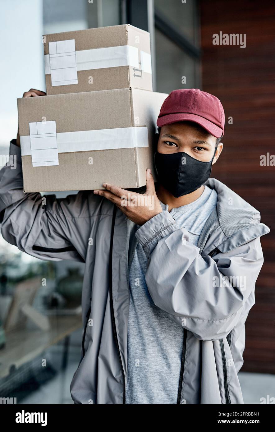 Keeping customers happy at a safe distance. a masked young man delivering a package to a place of residence. Stock Photo