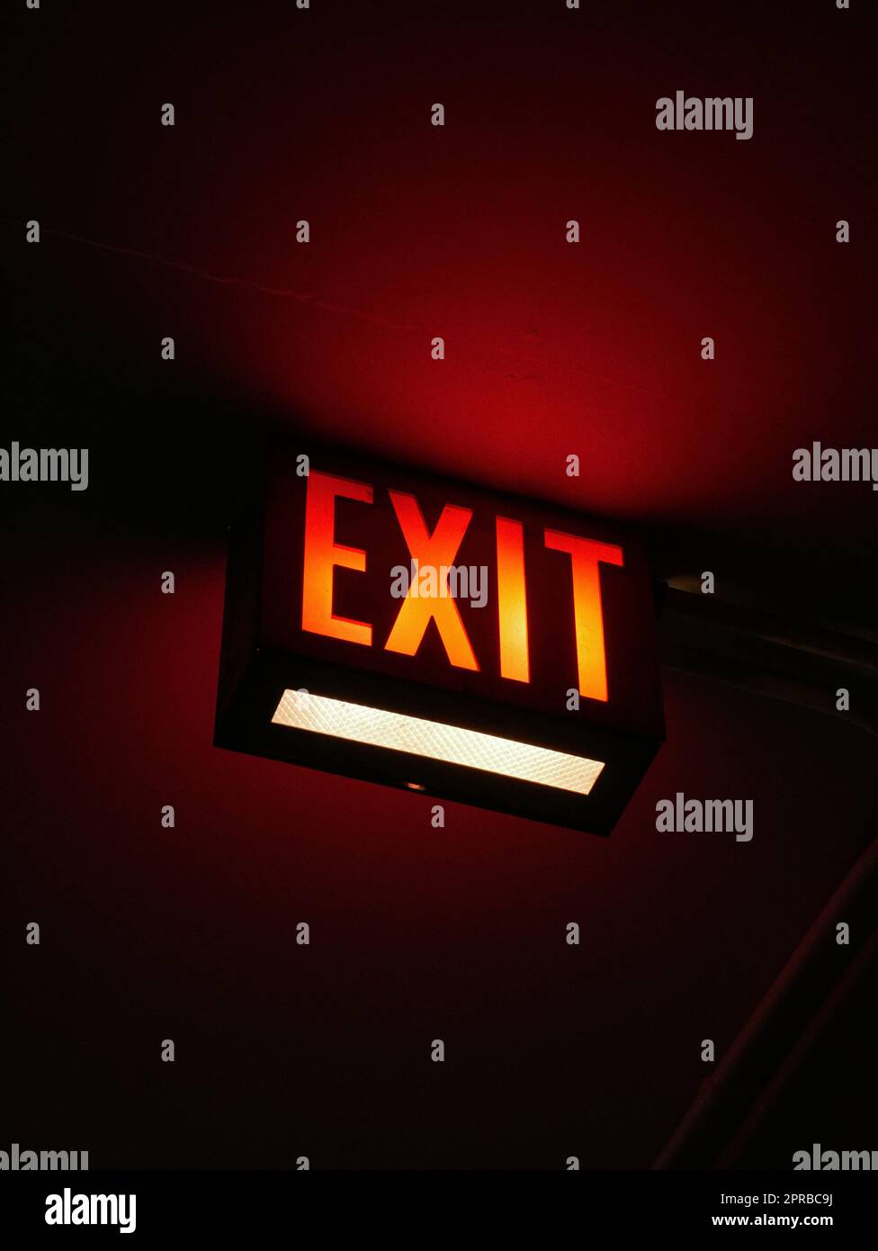 A welllit exit sign illuminated in a dark setting against a wall Stock