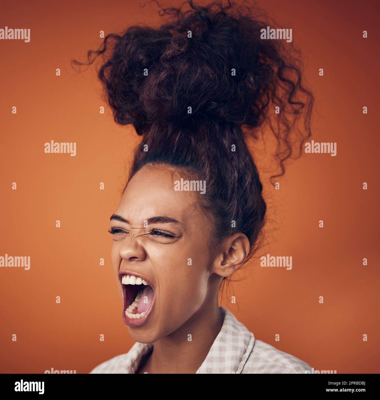Yes, my bun is as big as my mouth. a young woman wearing her hair in a bun against an orange background. Stock Photo